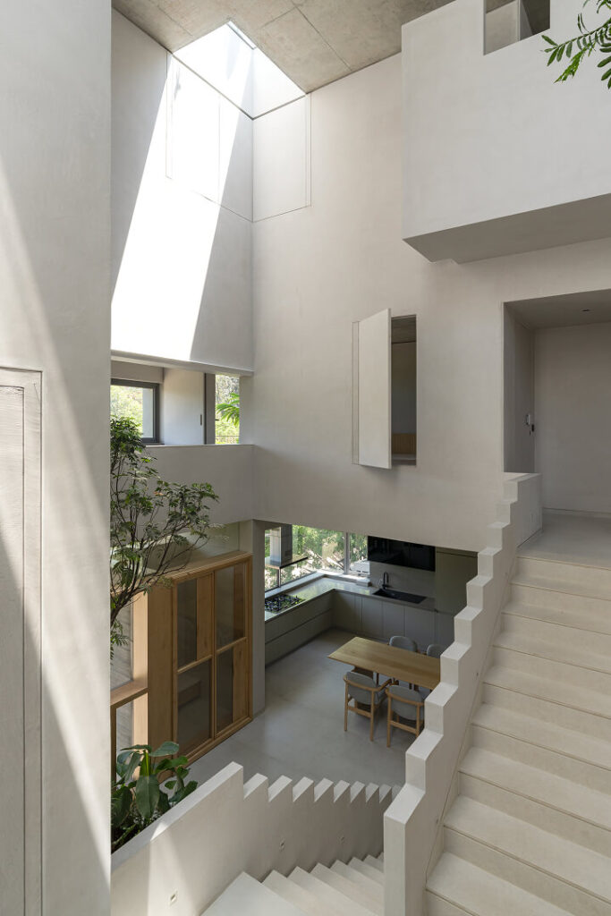 Sculptural raw-concrete staircase descending through the daylit heart of Stepwell House. Floor in Nexion Terraelino Gesso 120x240 cm